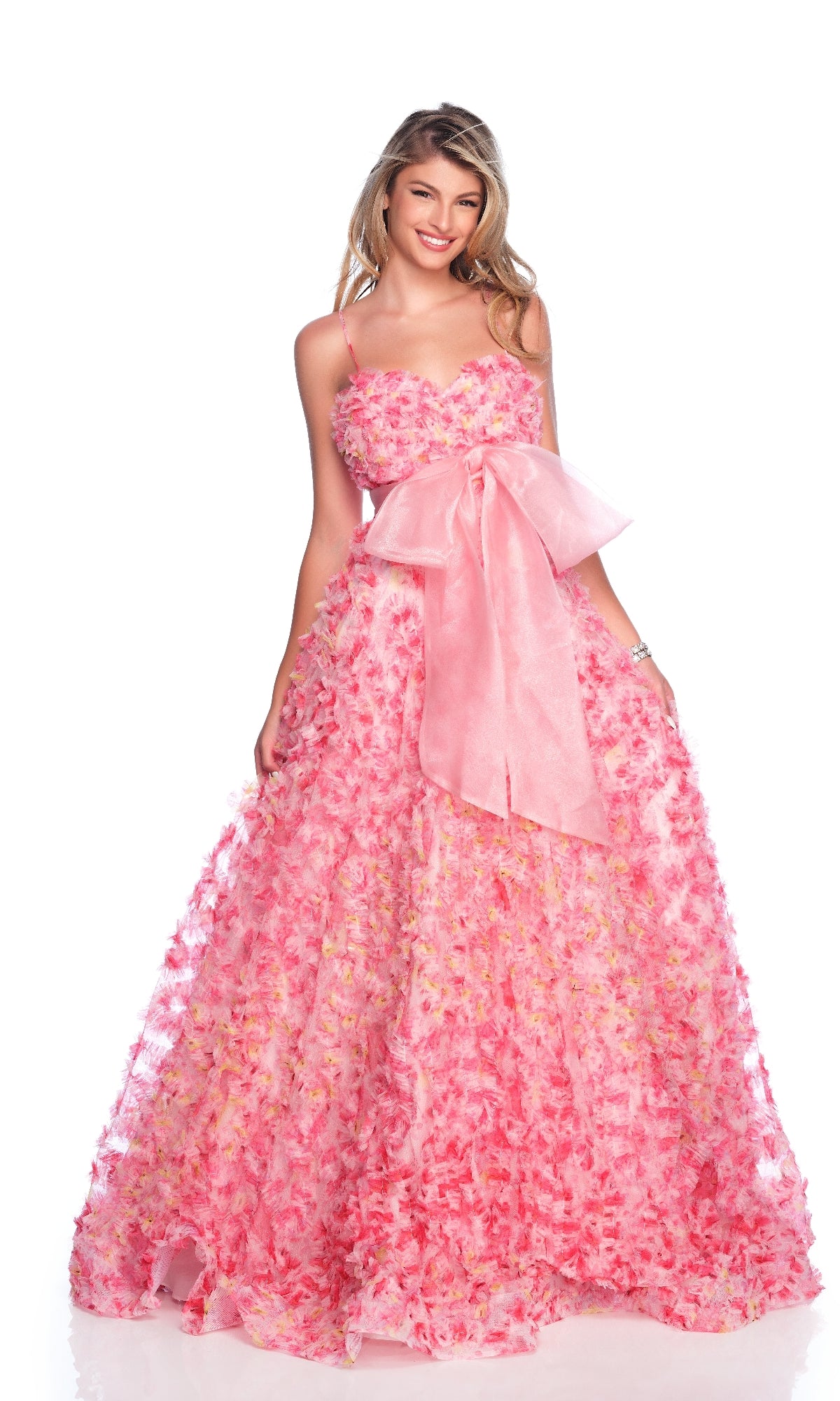 A woman poses and smiles in the Pink Print Bow Prom Ball Gown: Dave & Johnny 12136, a floor-length pink floral prom dress featuring an oversized pink waist bow, against a white background.